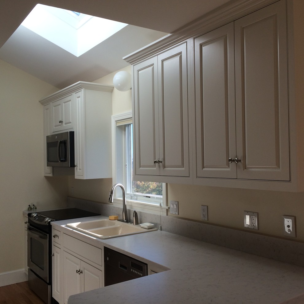 Photo of a mid-sized beach style galley eat-in kitchen in Portland Maine with a drop-in sink, raised-panel cabinets, white cabinets, quartz benchtops, stainless steel appliances, light hardwood floors and a peninsula.