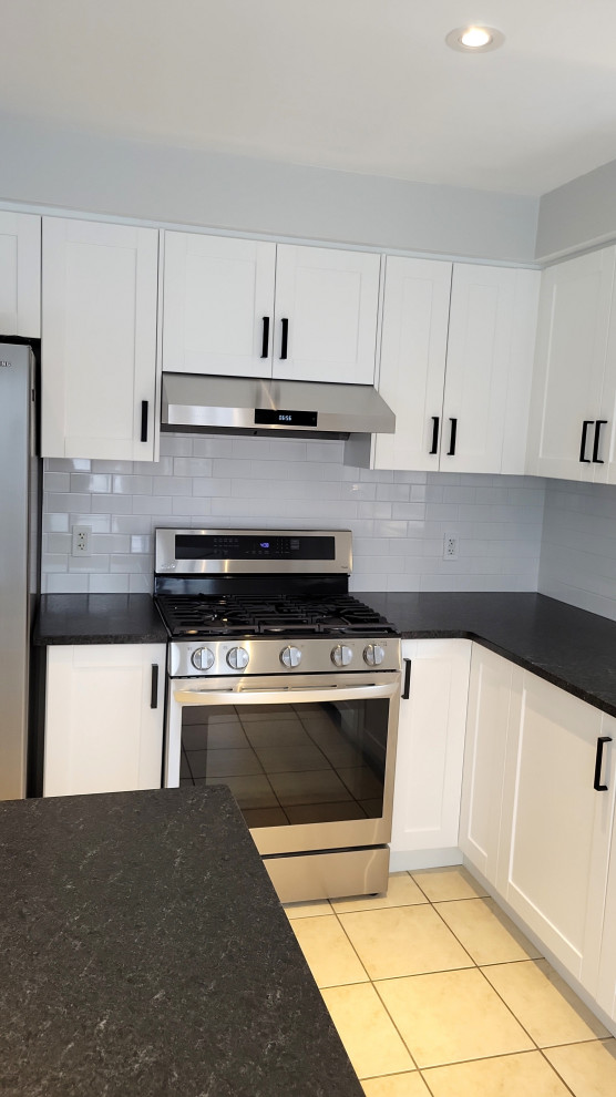 Example of a transitional kitchen design with an undermount sink, recessed-panel cabinets, white cabinets, granite countertops, gray backsplash, porcelain backsplash and black countertops