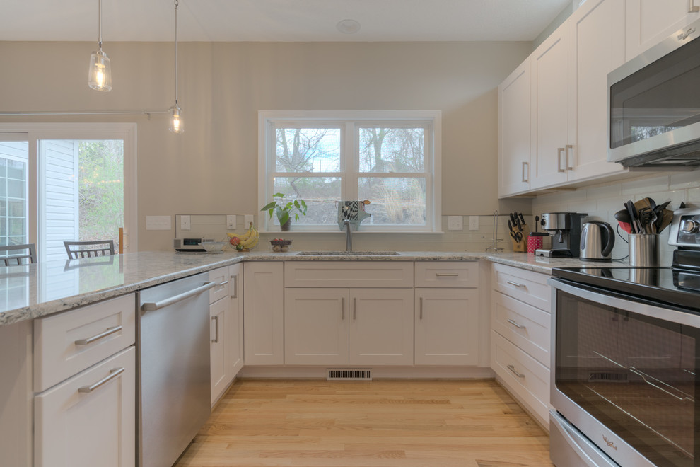 Example of a mid-sized transitional u-shaped light wood floor eat-in kitchen design with an undermount sink, shaker cabinets, white cabinets, quartz countertops, beige backsplash, glass tile backsplash, stainless steel appliances and a peninsula