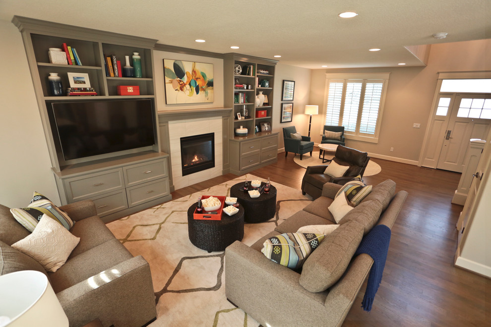 Photo of an expansive contemporary open concept family room in Portland with grey walls, medium hardwood floors, a standard fireplace, a tile fireplace surround and a wall-mounted tv.