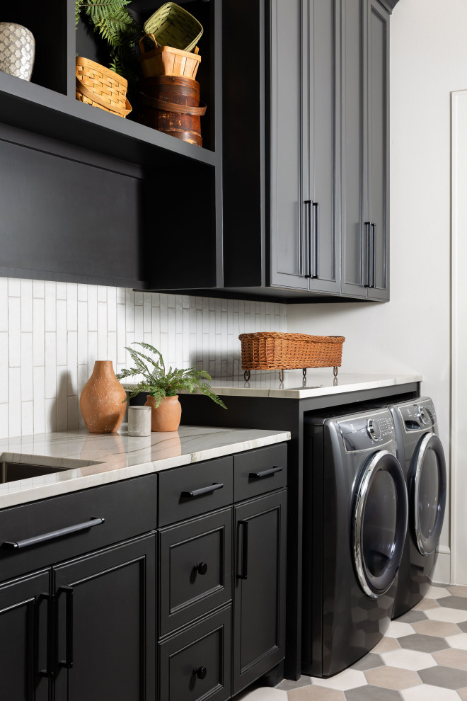 Mid-sized transitional galley dedicated laundry room in Dallas with an undermount sink, recessed-panel cabinets, black cabinets, quartzite benchtops, white splashback, ceramic splashback, white walls, porcelain floors, a side-by-side washer and dryer, multi-coloured floor and grey benchtop.
