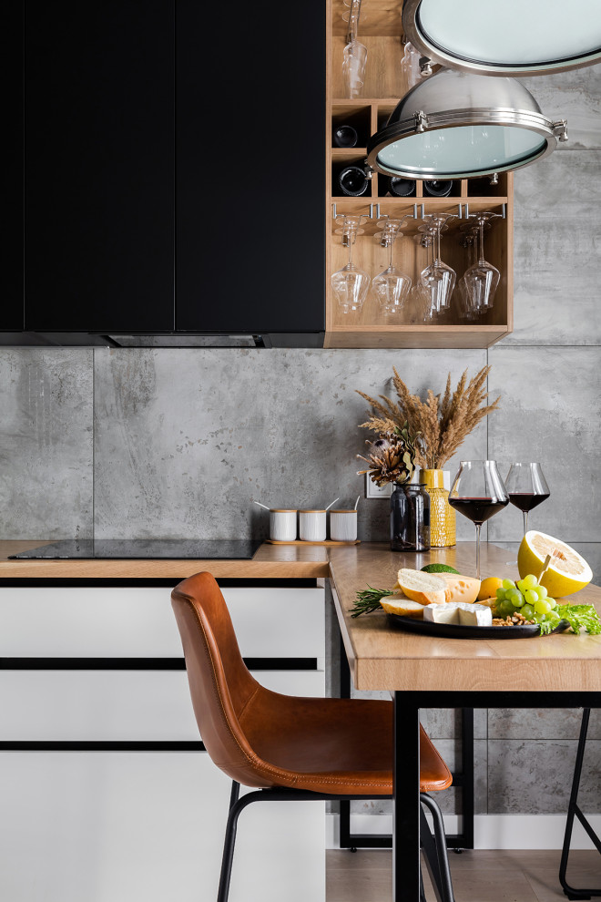 Small contemporary l-shaped eat-in kitchen in Saint Petersburg with an undermount sink, flat-panel cabinets, black cabinets, wood benchtops, grey splashback, porcelain splashback, black appliances, laminate floors, no island, beige floor and beige benchtop.