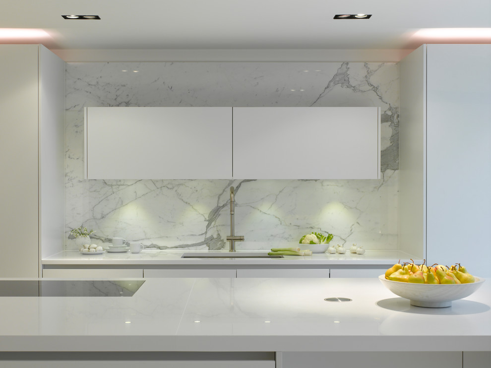 Design ideas for a large contemporary single-wall open plan kitchen in London with flat-panel cabinets, white cabinets, solid surface benchtops, white splashback, marble splashback, panelled appliances, with island, beige floor and white benchtop.