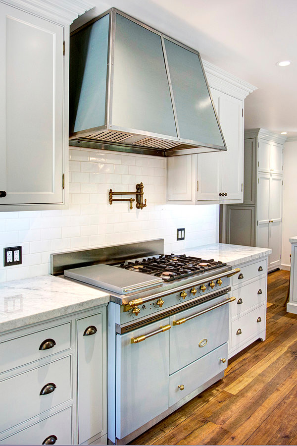 Photo of a large traditional galley eat-in kitchen in Los Angeles with a farmhouse sink, glass-front cabinets, white cabinets, quartzite benchtops, white splashback, porcelain splashback, panelled appliances, medium hardwood floors and with island.