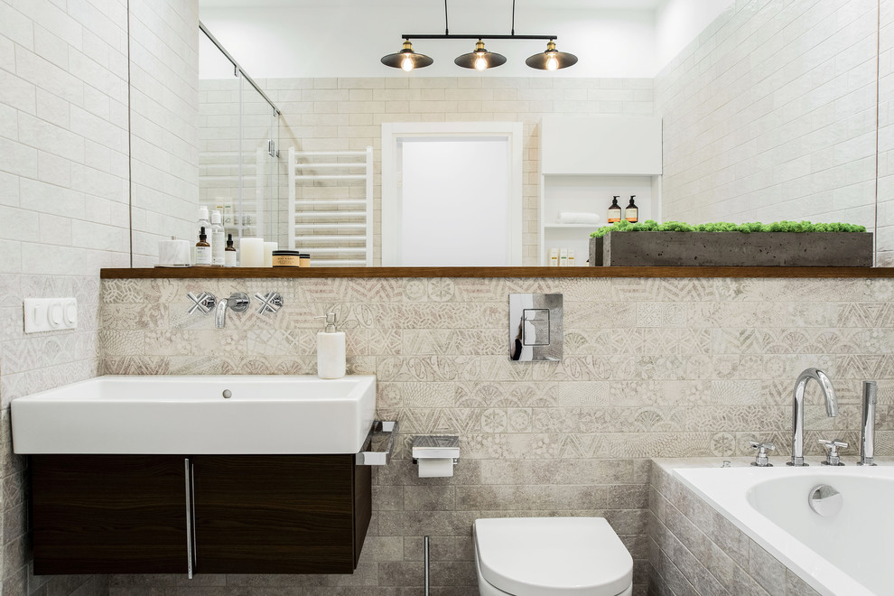 This is an example of a contemporary master bathroom in Other with flat-panel cabinets, an alcove tub, an alcove shower, beige tile, gray tile, a sliding shower screen, dark wood cabinets, a wall-mount toilet, white walls and a console sink.