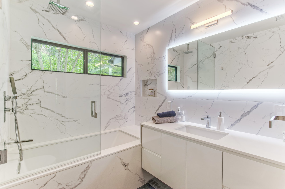 Design ideas for a mid-sized contemporary master bathroom in Los Angeles with flat-panel cabinets, white cabinets, a shower/bathtub combo, porcelain tile, porcelain floors, engineered quartz benchtops, grey floor, a hinged shower door, white benchtops, an undermount tub, white tile, white walls and an undermount sink.