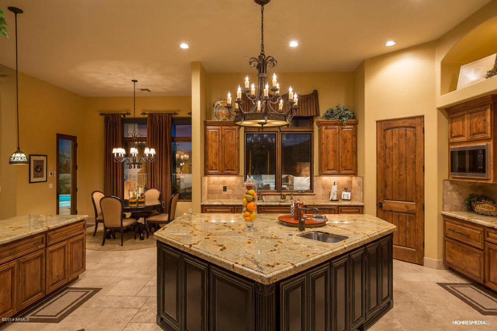 Example of a large transitional travertine floor open concept kitchen design in Phoenix with an undermount sink, raised-panel cabinets, medium tone wood cabinets, granite countertops, beige backsplash, stone tile backsplash, paneled appliances and two islands