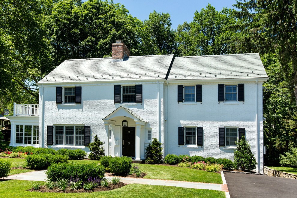 Large transitional two-storey brick white house exterior in New York with a gable roof and a shingle roof.