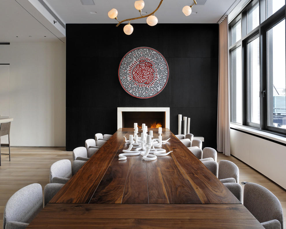 Photo of a modern dining room in New York with black walls, a standard fireplace and light hardwood floors.