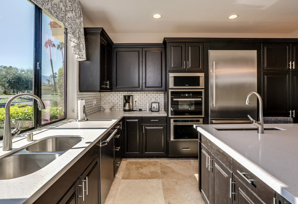 Eat-in kitchen - mid-sized transitional u-shaped travertine floor and brown floor eat-in kitchen idea with an undermount sink, raised-panel cabinets, black cabinets, quartz countertops, white backsplash, subway tile backsplash, stainless steel appliances, an island and gray countertops