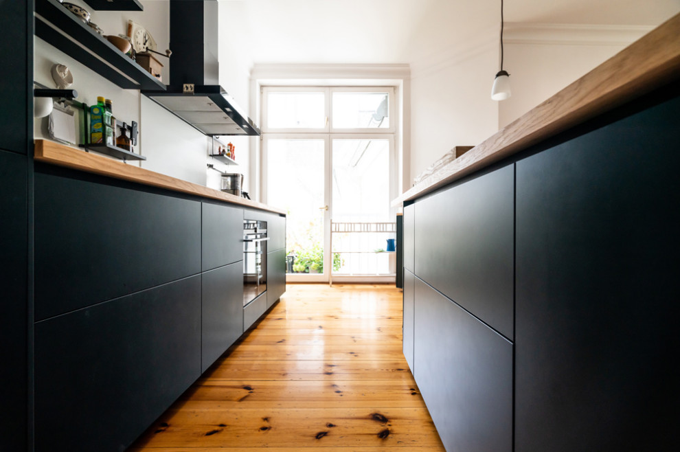 Foto di una grande cucina moderna con lavello a vasca singola, ante lisce, top in legno, paraspruzzi bianco, elettrodomestici neri, parquet chiaro, pavimento marrone e top marrone