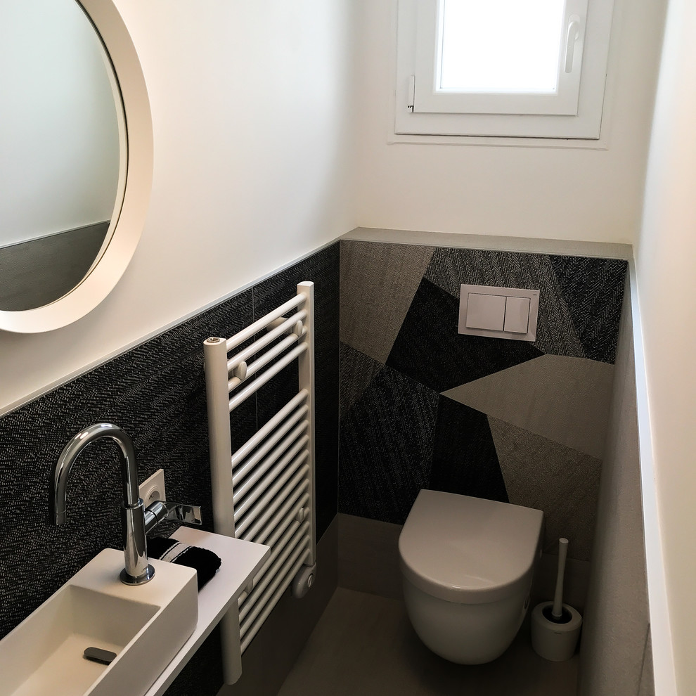 Inspiration for a small beach style powder room in Bordeaux with a wall-mount toilet, gray tile, white walls, a wall-mount sink and grey floor.