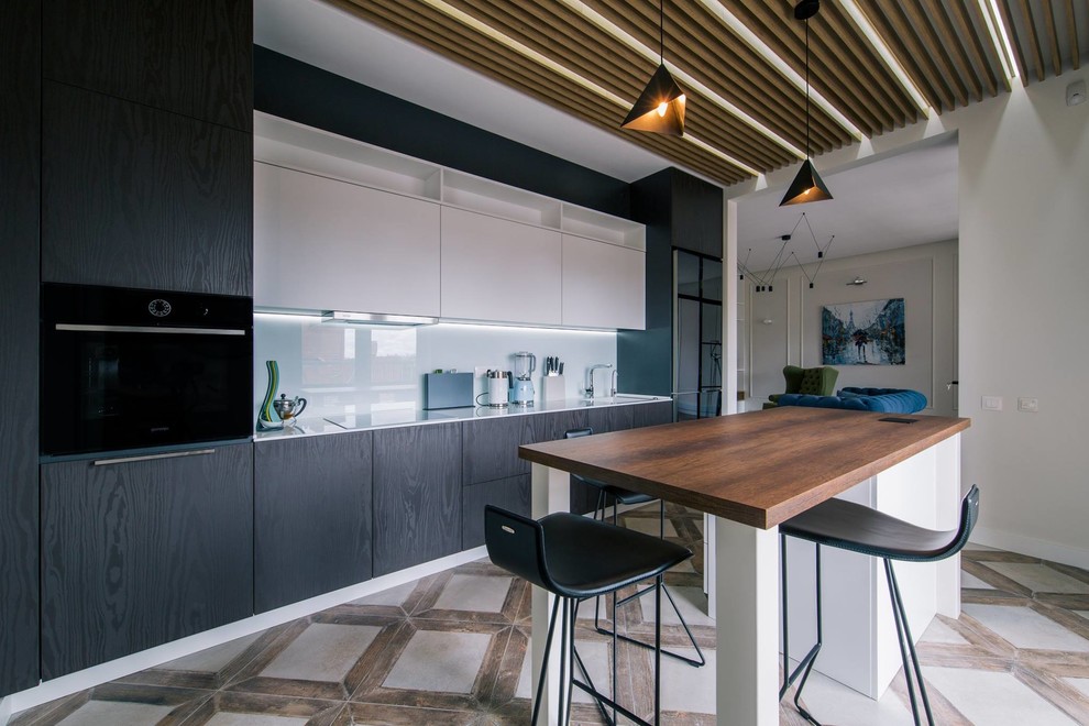 Mid-sized contemporary single-wall eat-in kitchen with an integrated sink, flat-panel cabinets, black cabinets, solid surface benchtops, white splashback, glass sheet splashback, black appliances, porcelain floors, with island, grey floor and white benchtop.