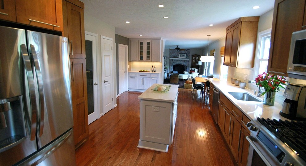 Inspiration for a mid-sized transitional galley medium tone wood floor and brown floor kitchen remodel in DC Metro with an undermount sink, shaker cabinets, medium tone wood cabinets, solid surface countertops, white backsplash, subway tile backsplash, stainless steel appliances, beige walls and an island