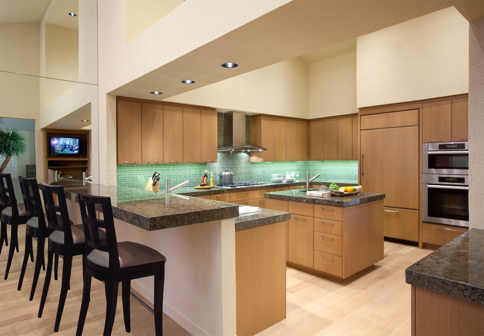 Design ideas for a contemporary u-shaped kitchen in Los Angeles with flat-panel cabinets, panelled appliances, medium wood cabinets, green splashback and matchstick tile splashback.