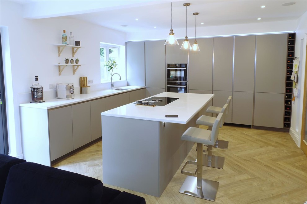 Photo of a large scandinavian open plan kitchen in Kent with grey cabinets, quartzite benchtops, white splashback, black appliances, with island and white benchtop.