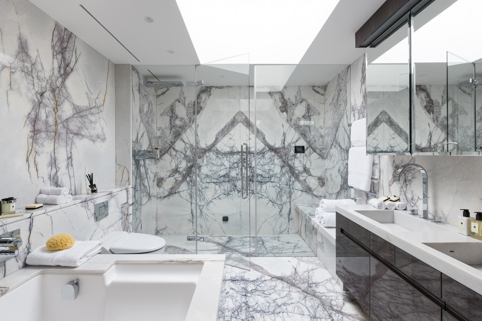 This is an example of a contemporary master bathroom in London with flat-panel cabinets, brown cabinets, an undermount tub, an alcove shower, a wall-mount toilet, marble, white walls, marble floors, an integrated sink, white floor and a hinged shower door.