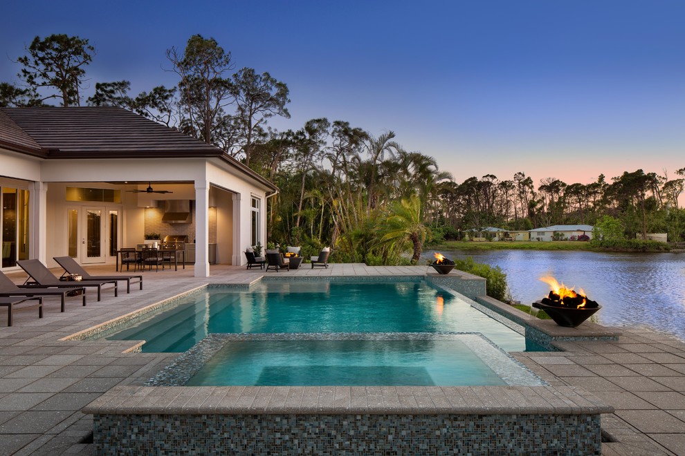 This is an example of an expansive tropical backyard custom-shaped infinity pool in Miami with a hot tub and concrete pavers.