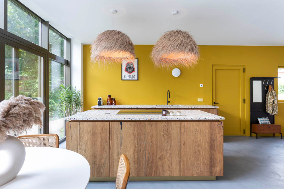 Large galley open plan kitchen in Paris with an undermount sink, beaded inset cabinets, dark wood cabinets, terrazzo benchtops, yellow splashback, panelled appliances, concrete floors, with island, grey floor and white benchtop.