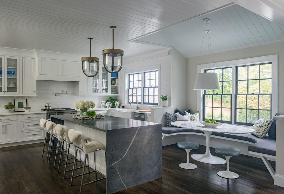 Photo of a beach style eat-in kitchen in Boston with a farmhouse sink, recessed-panel cabinets, white cabinets, white splashback, stainless steel appliances, dark hardwood floors, with island and brown floor.