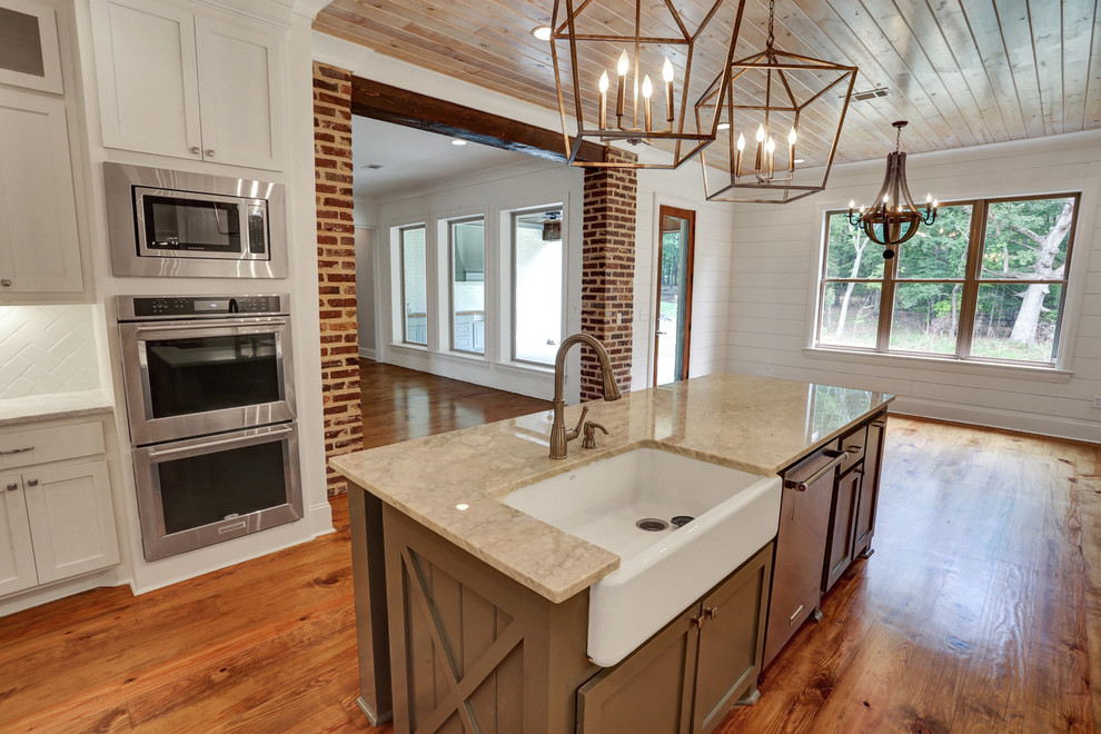 Design ideas for a mid-sized country u-shaped eat-in kitchen in Jackson with a farmhouse sink, shaker cabinets, white cabinets, white splashback, subway tile splashback, stainless steel appliances, medium hardwood floors, with island, brown floor and beige benchtop.