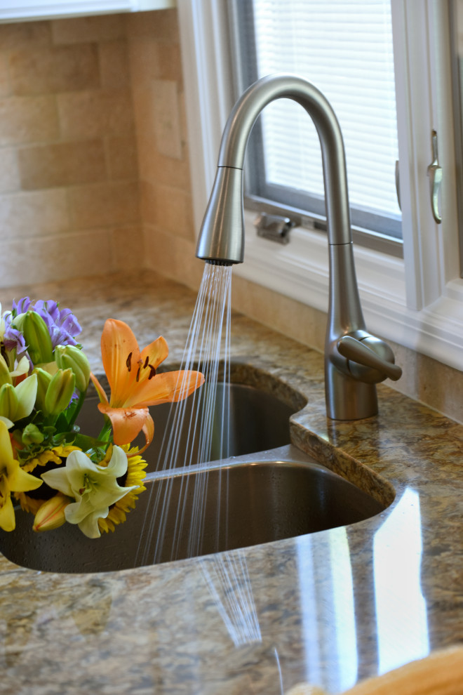 Example of a mid-sized transitional u-shaped porcelain tile, beige floor and tray ceiling enclosed kitchen design with an undermount sink, flat-panel cabinets, beige cabinets, quartz countertops, beige backsplash, travertine backsplash, black appliances, an island and beige countertops