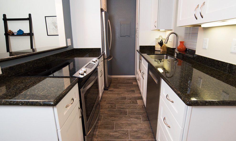 Small contemporary galley separate kitchen in Seattle with an undermount sink, shaker cabinets, white cabinets, granite benchtops, brown splashback, stone slab splashback, stainless steel appliances and ceramic floors.