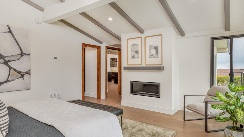 Photo of a mid-sized midcentury master bedroom in San Diego with white walls, medium hardwood floors, a standard fireplace, a plaster fireplace surround, brown floor and exposed beam.