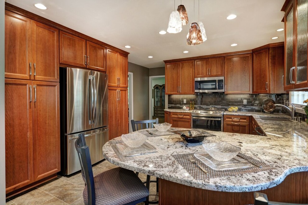 Mid-sized transitional l-shaped vinyl floor enclosed kitchen photo in Milwaukee with an undermount sink, raised-panel cabinets, medium tone wood cabinets, granite countertops, gray backsplash, glass tile backsplash and stainless steel appliances