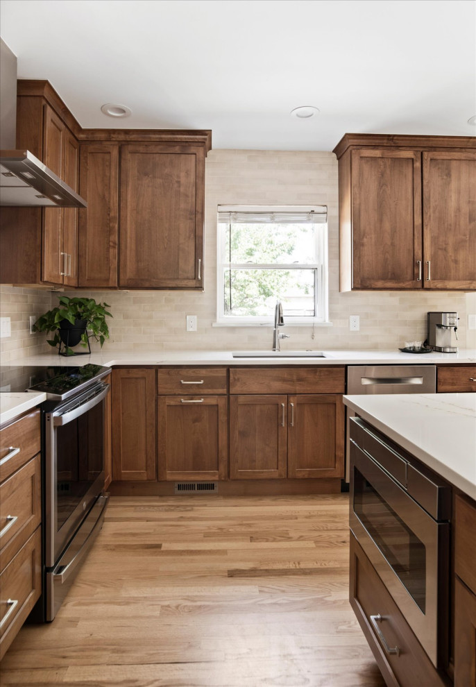 Example of a small transitional l-shaped light wood floor and brown floor eat-in kitchen design in Denver with an undermount sink, shaker cabinets, medium tone wood cabinets, beige backsplash, stainless steel appliances, an island and white countertops