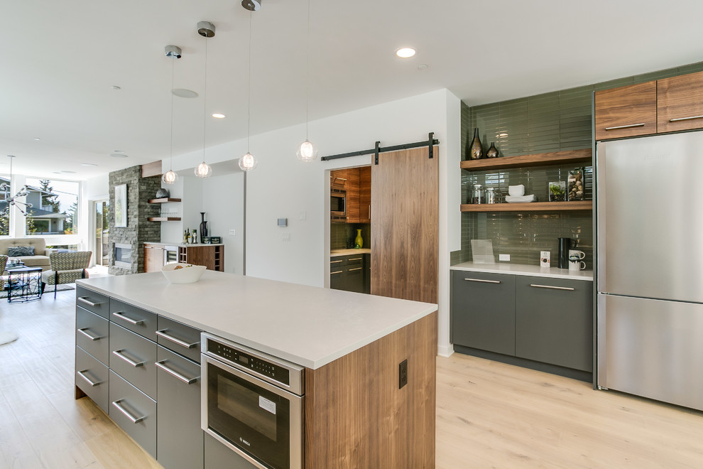 Inspiration for a large contemporary kitchen pantry in Seattle with an undermount sink, flat-panel cabinets, grey cabinets, solid surface benchtops, green splashback, glass tile splashback, stainless steel appliances, light hardwood floors, with island and beige floor.