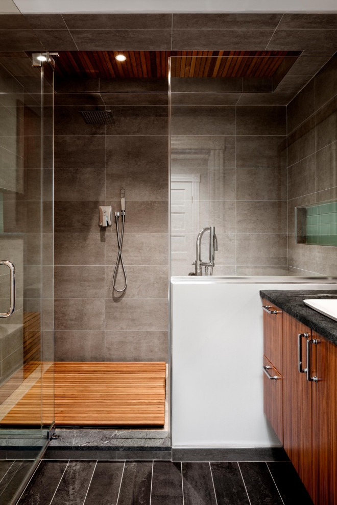 This is an example of a large contemporary master wet room bathroom in DC Metro with flat-panel cabinets, brown cabinets, a freestanding tub, gray tile, ceramic tile, beige walls, ceramic floors, a drop-in sink, marble benchtops, grey floor, an open shower, black benchtops, a shower seat, a single vanity, a floating vanity, recessed and wood walls.