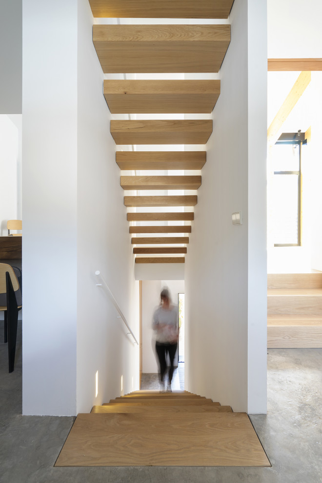 На фото: большая прямая лестница в современном стиле с деревянными ступенями, металлическими перилами и панелями на части стены без подступенок
