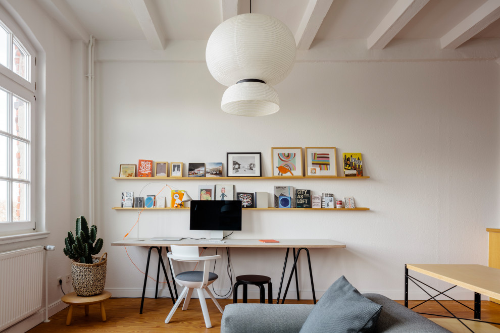 Modernes Arbeitszimmer mit weißer Wandfarbe, braunem Holzboden, freistehendem Schreibtisch, braunem Boden und freigelegten Dachbalken in Hamburg