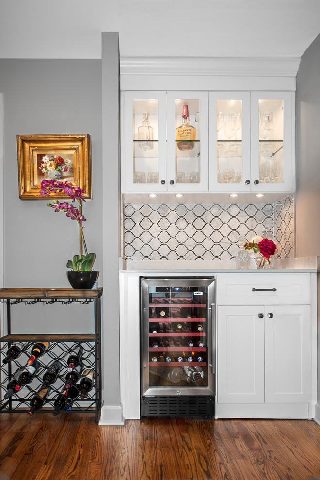 Design ideas for a small transitional single-wall home bar in Chicago with no sink, recessed-panel cabinets, white cabinets, medium hardwood floors, brown floor and multi-coloured benchtop.