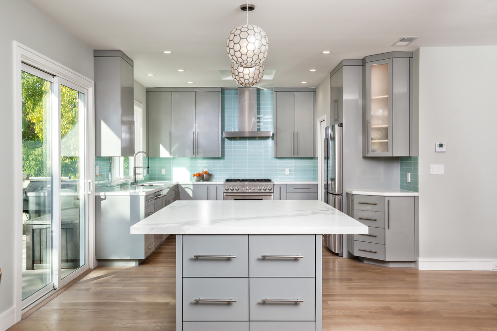 This is an example of a mid-sized contemporary u-shaped kitchen in San Francisco with an undermount sink, flat-panel cabinets, grey cabinets, blue splashback, stainless steel appliances, medium hardwood floors, with island, quartzite benchtops, glass tile splashback and brown floor.