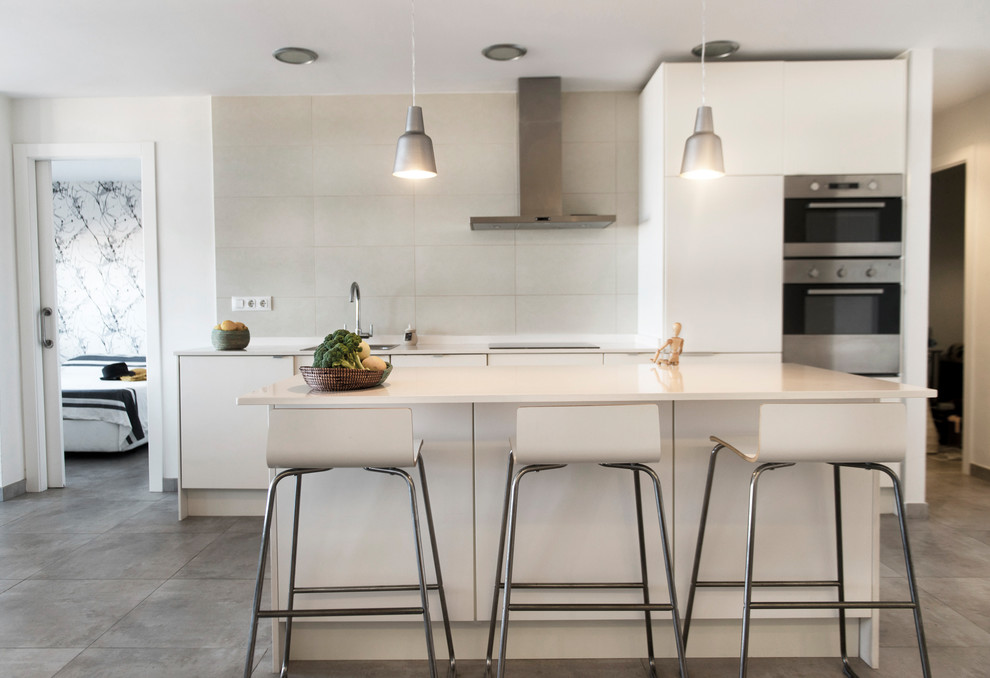 Inspiration for a mid-sized contemporary single-wall open plan kitchen in Valencia with flat-panel cabinets, white cabinets, white splashback, stainless steel appliances, with island, grey floor and white benchtop.