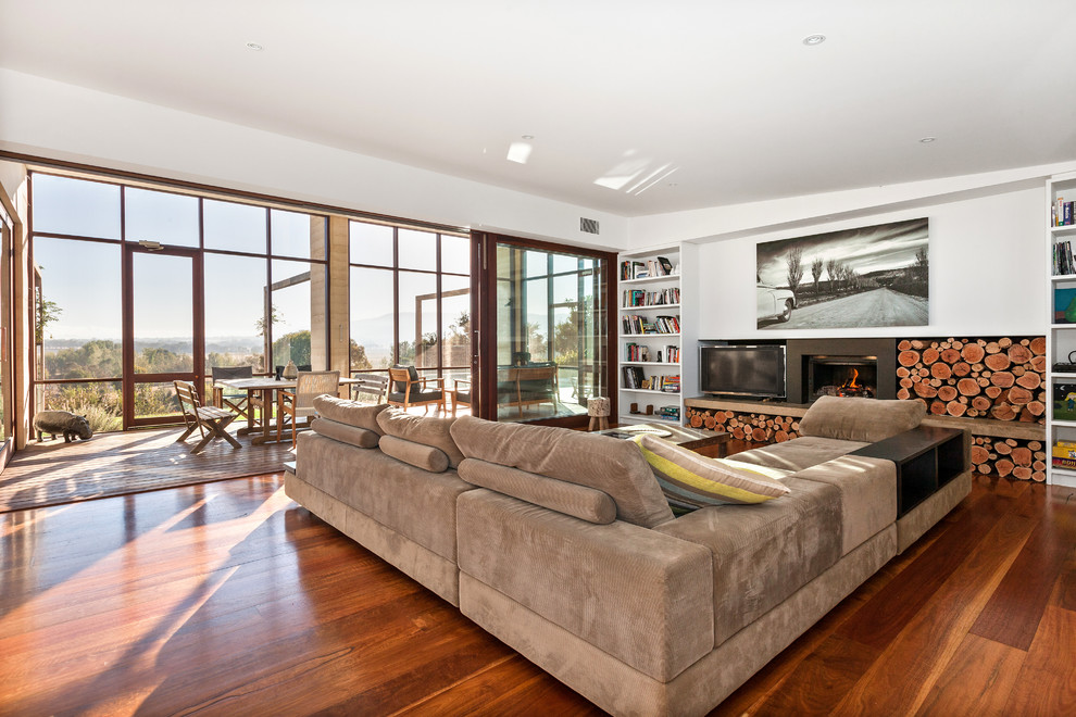 This is an example of a contemporary living room in Other with white walls, medium hardwood floors, a standard fireplace, a freestanding tv and brown floor.
