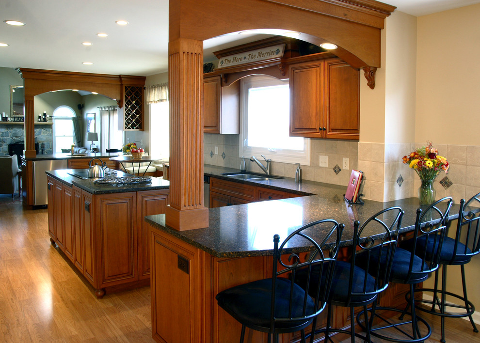This is an example of a mid-sized traditional l-shaped eat-in kitchen in Philadelphia with a double-bowl sink, raised-panel cabinets, medium wood cabinets, beige splashback, ceramic splashback, stainless steel appliances, medium hardwood floors and with island.
