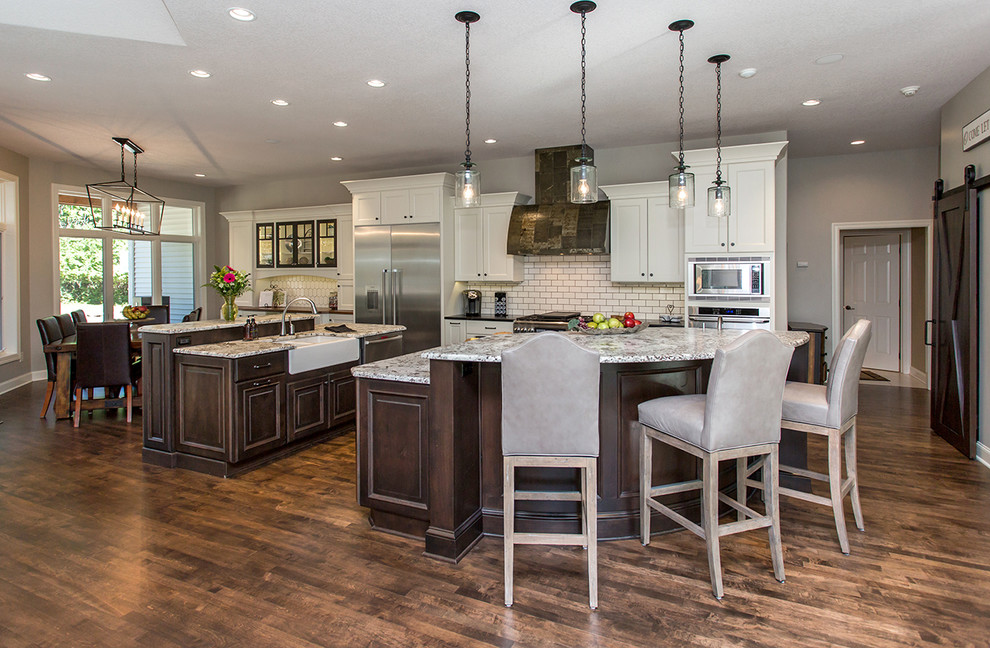 Kitchen - huge transitional medium tone wood floor kitchen idea with a farmhouse sink, flat-panel cabinets, white backsplash, ceramic backsplash, stainless steel appliances, two islands and granite countertops