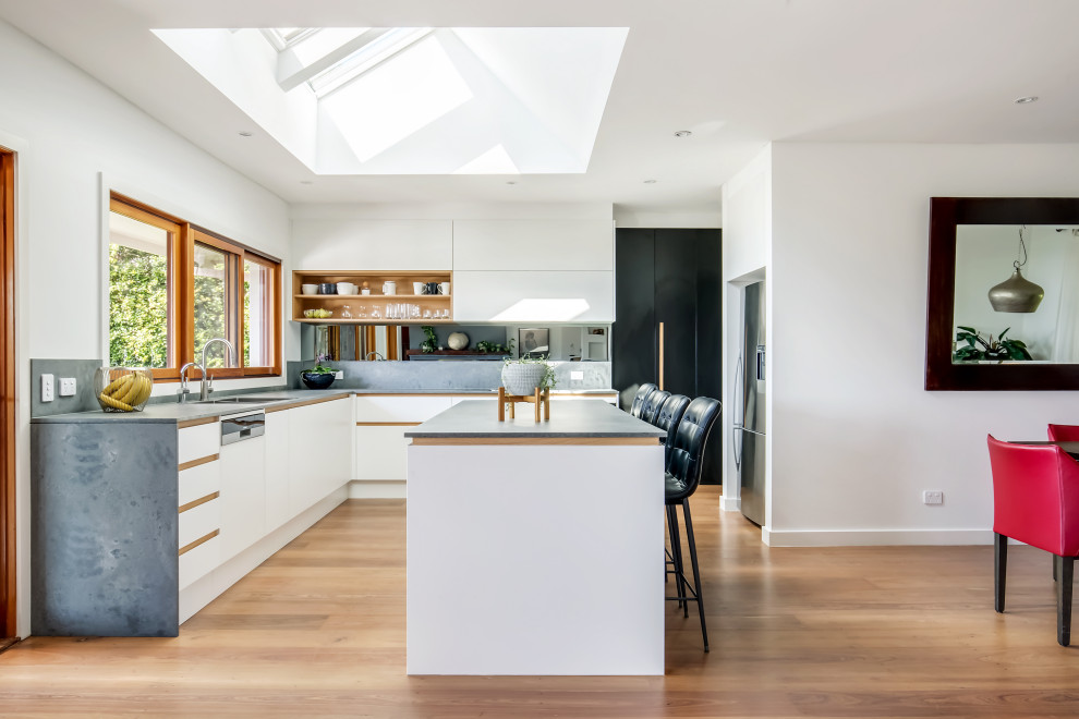 Inspiration for a large contemporary l-shaped open plan kitchen in Sydney with an undermount sink, flat-panel cabinets, white cabinets, quartz benchtops, grey splashback, engineered quartz splashback, black appliances, medium hardwood floors, with island and grey benchtop.