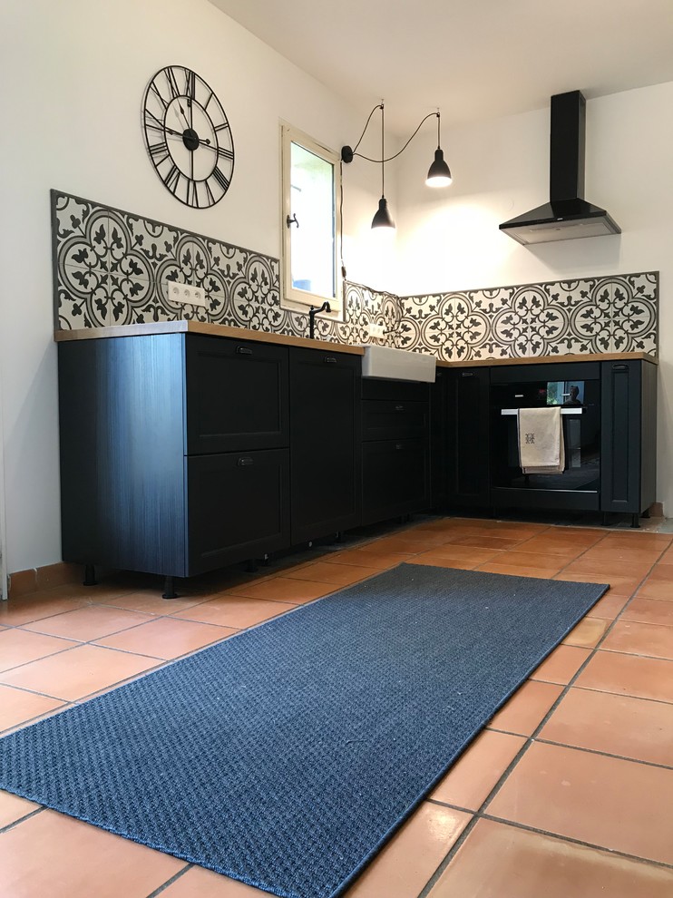 Photo of a mid-sized midcentury l-shaped open plan kitchen in Marseille with an undermount sink, beaded inset cabinets, dark wood cabinets, wood benchtops, multi-coloured splashback, cement tile splashback, black appliances, terra-cotta floors, no island and orange floor.