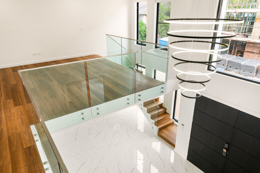 Cette image montre un grand escalier minimaliste en L avec des marches en bois, des contremarches en verre et un garde-corps en métal.