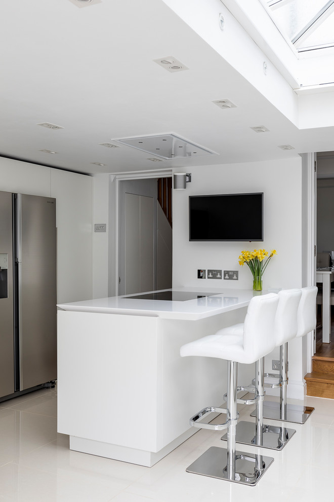 This is an example of a mid-sized contemporary galley separate kitchen in London with an undermount sink, flat-panel cabinets, white cabinets, glass benchtops, blue splashback, glass sheet splashback, stainless steel appliances, porcelain floors, with island, white floor and white benchtop.