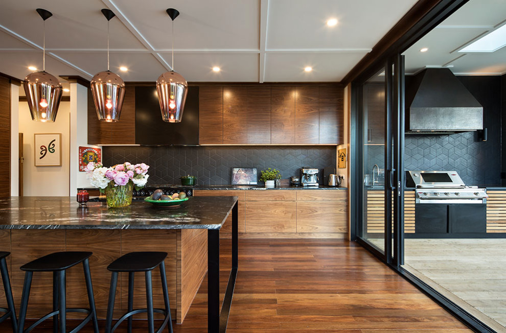 Inspiration for a large midcentury l-shaped eat-in kitchen in Auckland with a double-bowl sink, raised-panel cabinets, medium wood cabinets, granite benchtops, black splashback, ceramic splashback, black appliances, with island and black benchtop.