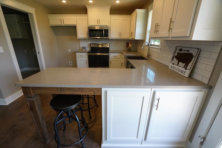 Example of a large transitional u-shaped medium tone wood floor and brown floor eat-in kitchen design with a farmhouse sink, shaker cabinets, white cabinets, quartzite countertops, white backsplash, subway tile backsplash, stainless steel appliances and a peninsula