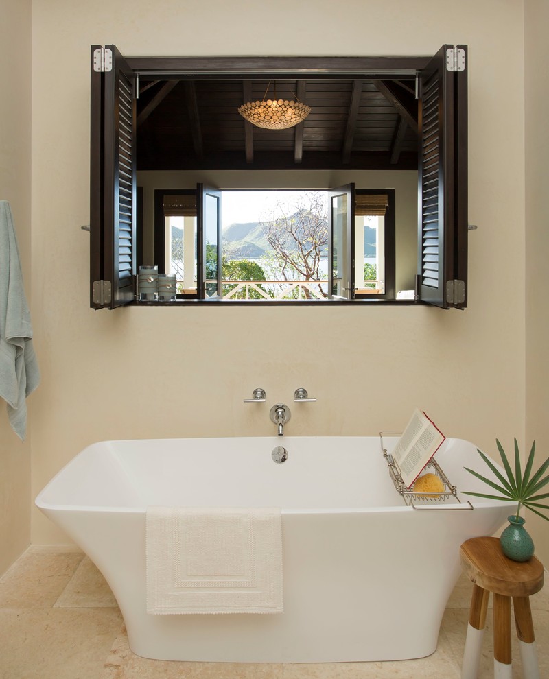 This is an example of a tropical master bathroom in Charleston with a freestanding tub, beige tile, stone tile and beige walls.