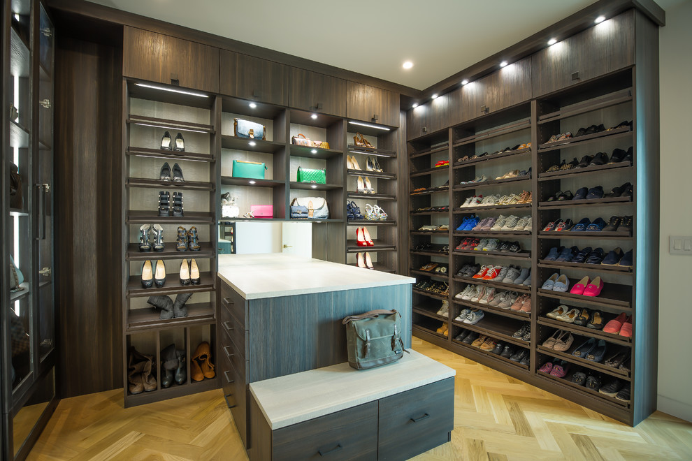 This is an example of an expansive contemporary gender-neutral dressing room in Los Angeles with flat-panel cabinets, dark wood cabinets, light hardwood floors and beige floor.