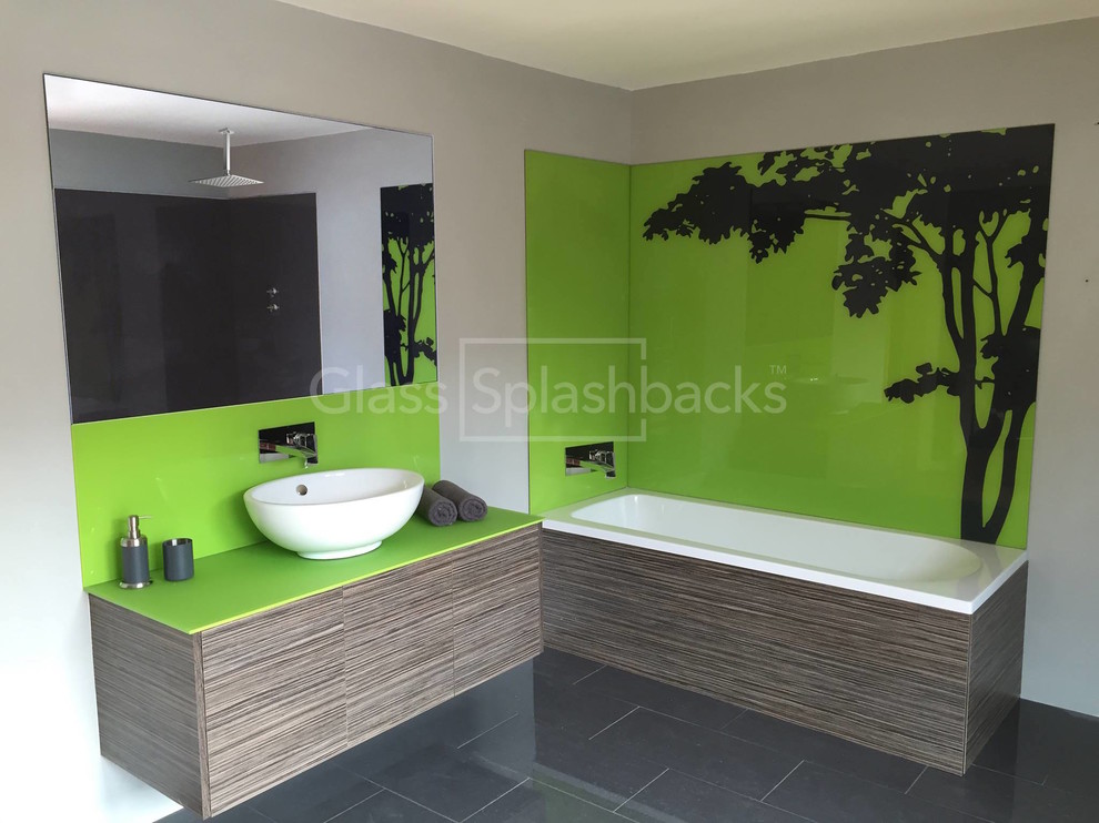Inspiration for a modern bathroom in Belfast with flat-panel cabinets, dark wood cabinets, a built-in bath, a walk-in shower, a wall mounted toilet, green tiles, glass sheet walls, grey walls and ceramic flooring.