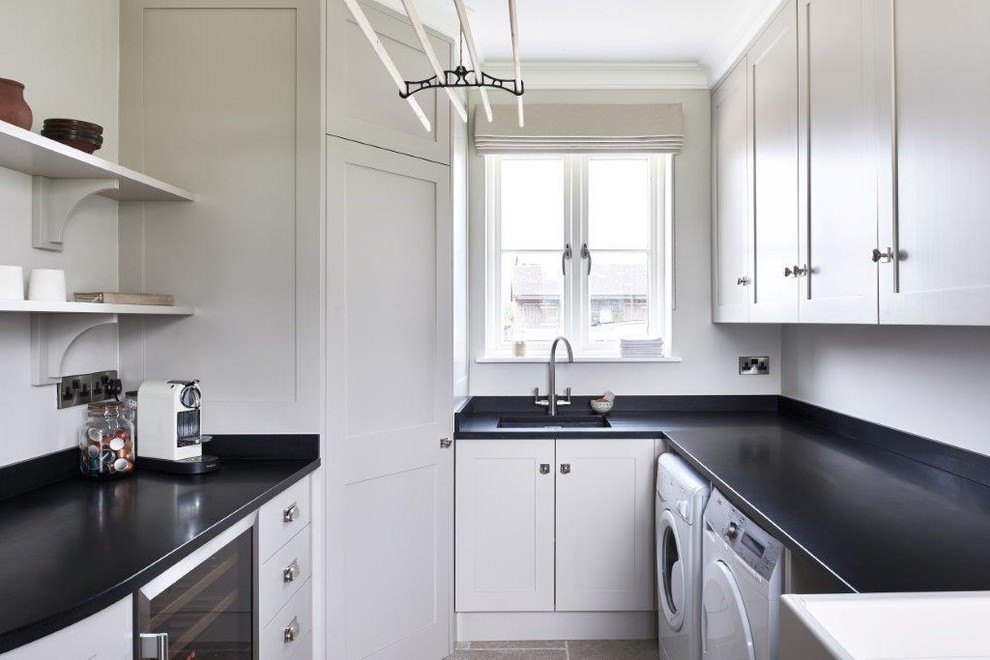 This is an example of a traditional u-shaped utility room in Wiltshire with a drop-in sink, shaker cabinets, grey cabinets, granite benchtops, travertine floors and a side-by-side washer and dryer.